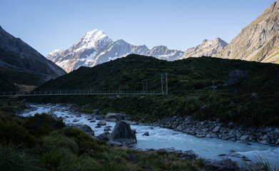Beautiful alpine valley with glacial river, swing bridge and snowy mountain, Mt Cook, New Zealand