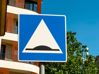 Traffic sign indicating speed bump displayed on a blue board along an urban street. Safety,...