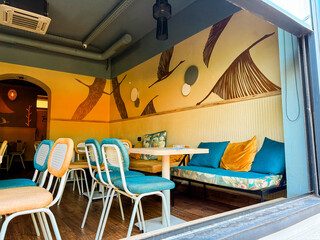 Interior of a cafe with colorful furniture, decorative pillows and painted bird motifs on the wall. Hospitality, leisure and lifestyle environment representing design, comfort and modern dining.