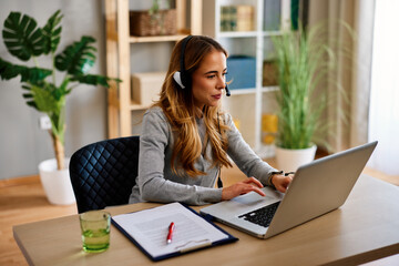 Young woman working from home office using laptop and headset
