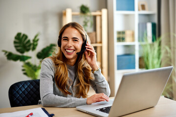 Obraz premium Happy female entrepreneur working remotely using laptop and headset in home office