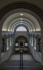 Fototapeta premium a grand staircase with a prominent wooden handrail leading towards a large arched window at the top, and is flanked by arched hallways on either side within the National Portrait Gallery in London.