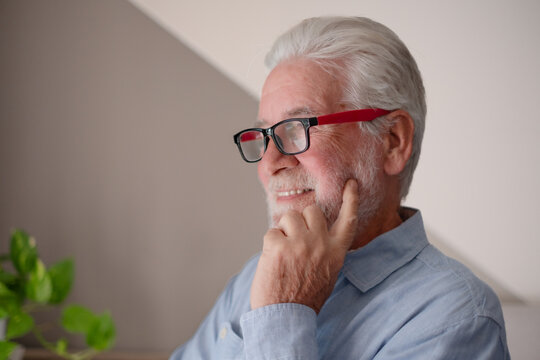 Portrait of smiling senior man in eyeglasses while looking away indoors radiating positivity and confidence. Concept of healthy aging, wisdom, lifestyle, vision, and happiness in old age