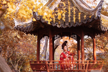 Fototapeta premium Woman in traditional red hanfu poses gracefully in an autumn garden pavilion Chinese word means autumn.