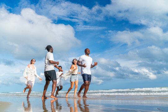Happy diverse man and woman walking and playing together on the beach in sunny day. Group of People friends enjoy and fun outdoor active lifestyle travel nature the sea on summer holiday vacation.