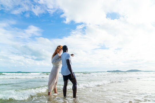 Happy man and woman travel nature the sea on summer beach holiday vacation. Diverse family couple enjoy outdoor active lifestyle walking and relaxing together on tropical island beach at summer sunset - Powered by Adobe