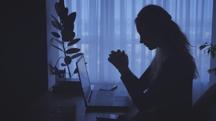dark unrecognizable silhouette unhappy tired woman working on laptop sitting at desk in black room window light. Sad girl suffers from headache depression fatigue lack of money, Person looking for job - Powered by Adobe