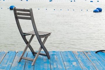a solitary wooden chair rests on a blue dock and gazing out over calm sea at horizontal composition