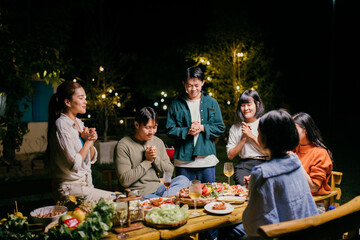 Asian friends praying before dinner party in garden at night