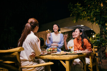 Asian friends enjoying dinner party, laughing and drinking wine at a table in the garden