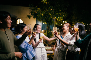Friends toasting with white wine at night party in the garden