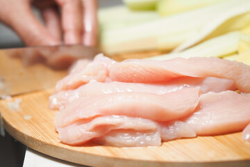 Slicing fresh chicken fillets on a wooden board in kitchen