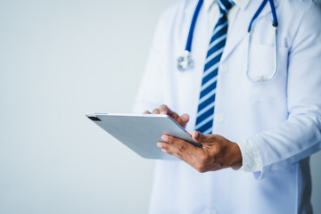 Doctor using tablet with stethoscope around neck wearing lab coat and tie