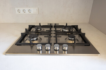 Stainless gas cooktop with four burners and cast-iron grates set into a modern kitchen countertop