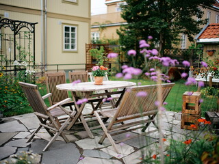 Charming Backyard Oasis with Wooden Patio Furniture Set Surrounded by Vibrant Blooming Flowers and Lush Greenery in a Cozy Outdoor Setting
