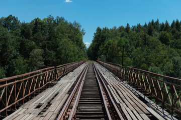 Obraz premium Straight railway track perspective on wooden bridge leading through forest canopy