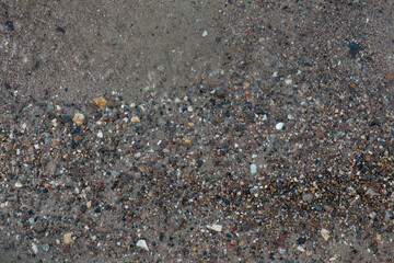 Close-up texture of wet sand and pebbles creating natural abstract pattern