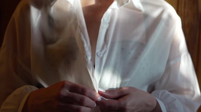 Woman buttoning shirt, sheer white blouse, getting dressed in an intimate morning routine