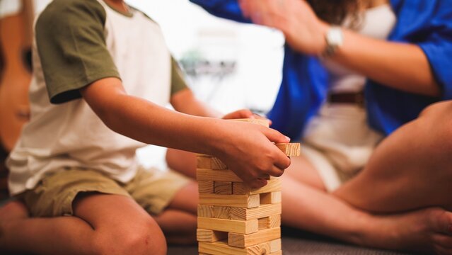 Child playing wooden block tower game with parent clapping in background
