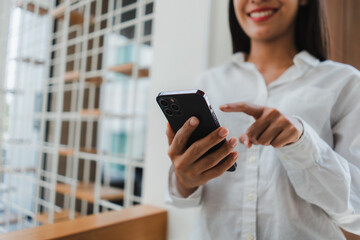 Close-up of a smiling businesswoman engaging with her smartphone, pointing at the screen while immersed in her work