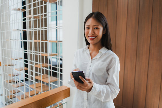 Smiling businesswoman using a smartphone while working in a modern office, enjoying a productive day in a bright, stylish environment