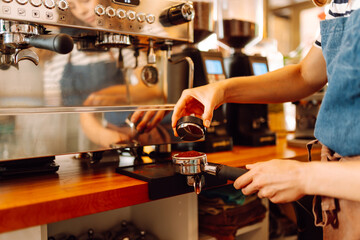 An experienced barista prepares aromatic coffee on a modern espresso machine. Hands of a woman frothing milk, preparing espresso in a cozy coffee shop. Small business concept, drinks.