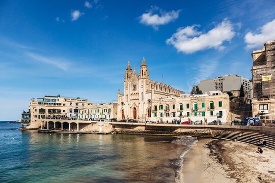 Balluta Bay, Malta &ndash; April 9, 2025: The neo-gothic Carmelite Church stands on the waterfront of Balluta Bay between St Julian's and Sliema, surrounded by traditional and modern buildings