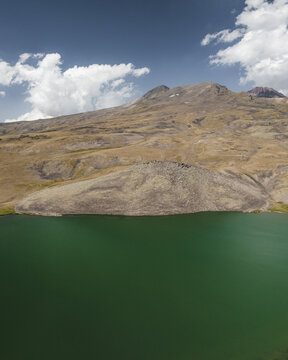 Aerial view of the tranquil lake reflecting a rugged mountain under a blue sky with scattered clouds, Lake Kari, Aragatsotn Province, Armenia.