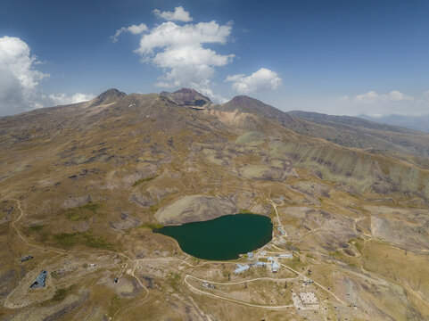 Aerial view of the emerald lake nestled beneath the stark, rocky peaks of Aragats Mountain under a vast sky, Lake Kari, Aragatsotn Province, Armenia.