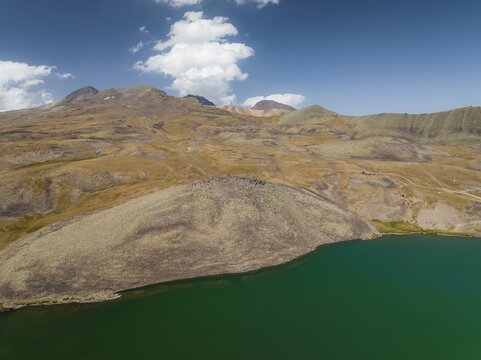 Aerial view of a turquoise lake nestled against the rugged, ochre-toned mountains under a bright blue sky, Lake Kari, Aragatsotn Province, Armenia.