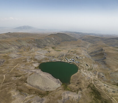 Aerial view of the dark, serene waters of Lake Kari nestled amidst the arid, mountainous terrain under a hazy sky, Lake Kari, Aragatsotn Province, Armenia.