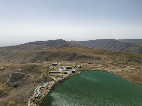 Aerial view of the tranquil turquoise lake mirroring the arid mountains, with buildings clustered along its edge, Lake Kari, Aragatsotn Province, Armenia.