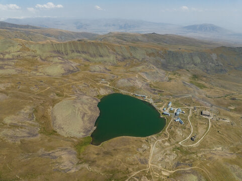 Aerial view of the emerald Lake Kari nestled amidst the rugged, sun-drenched Aragatsotn Province, with winding paths tracing the arid landscape, Lake Kari, Aragatsotn Province, Armenia.