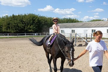 Little girl learning horseback riding with trainer on farm arena