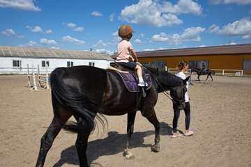 Little girl learning horseback riding with trainer on farm arena