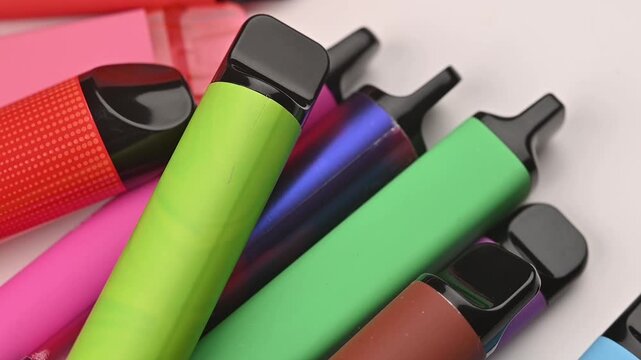 Colorful disposable vapes arranged close-up, modern electronic smoking devices in various bright colors. Rotating 