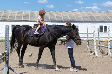Little girl learning horseback riding with trainer on farm arena