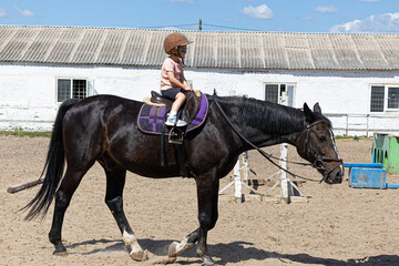 Little girl riding a horse alone in outdoor arena
