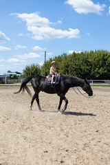 Little girl riding a horse alone in outdoor arena