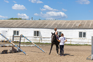 Child horse riding lesson with instructor in sunny outdoor equestrian arena