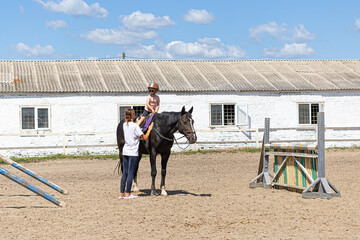 Child horse riding lesson with instructor in sunny outdoor equestrian arena