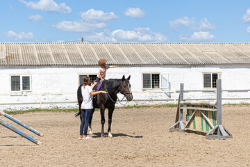 Child horse riding lesson with instructor in sunny outdoor equestrian arena