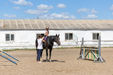 Child horse riding lesson with instructor in sunny outdoor equestrian arena