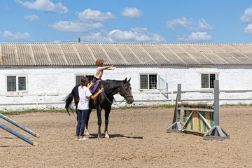 Child horse riding lesson with instructor in sunny outdoor equestrian arena