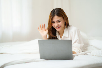 Young woman waving during video call on laptop in bed