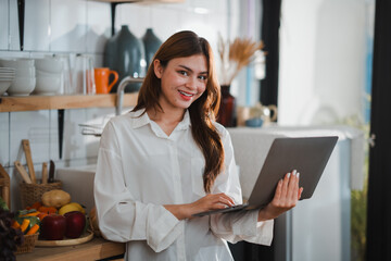 Smiling young woman using laptop in kitchen with fresh produce