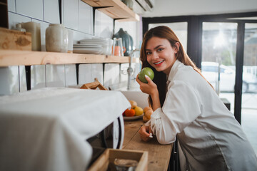 Young woman holding a green apple, smiling in her kitchen