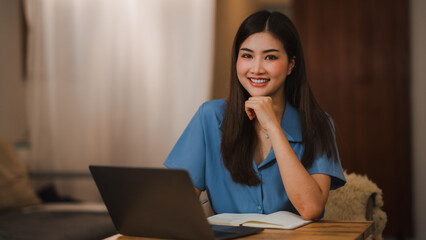Smiling Asian businesswoman working from home using laptop at night
