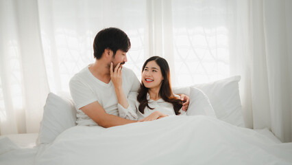 Happy asian couple cuddling in bed enjoying intimacy and tenderness
