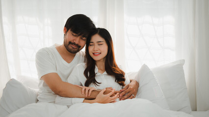 Asian couple embracing on bed in cozy bedroom